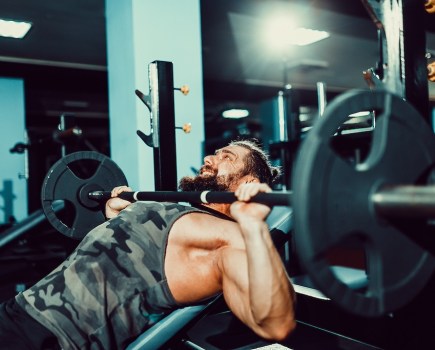 man in vest doing incline bench press in the gym to show time under tension
