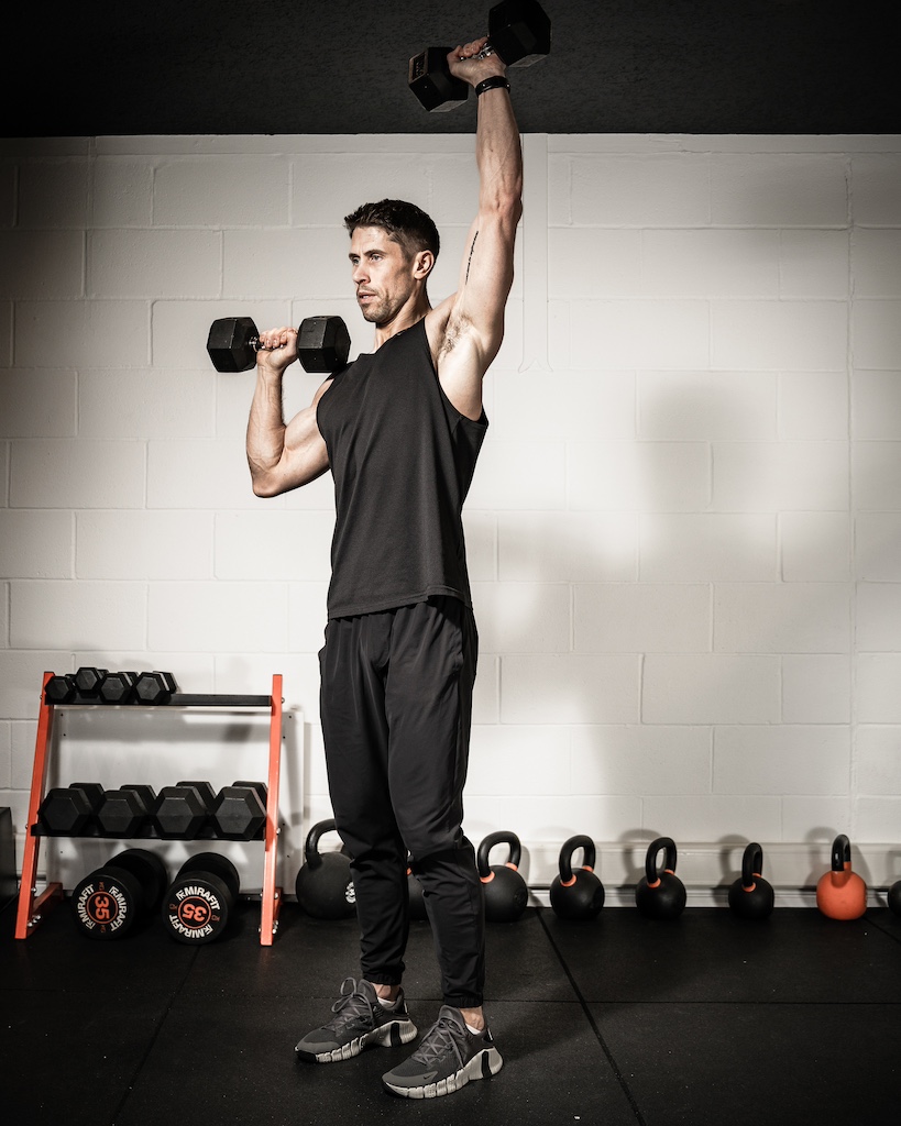 Personal trainer demonstrating how to do a dumbbell alternating shoulder press as part of a metabolic resistance training workout