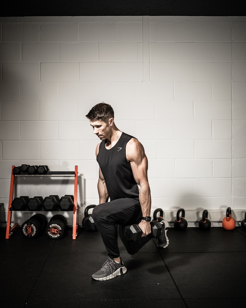 Personal trainer demonstrating how to do a dumbbell reverse lunge