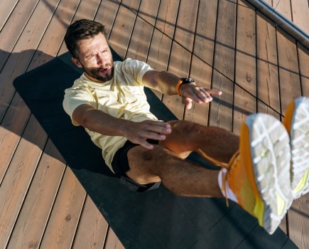 A man focused on his core workout, performing a V-sit exercise on a yoga mat outdoors.