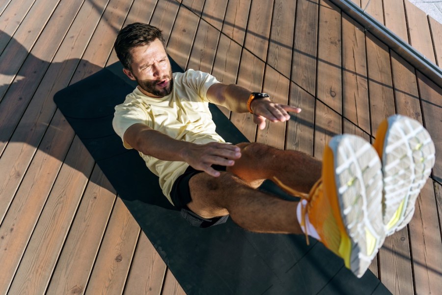 A man focused on his core workout, performing a V-sit exercise on a yoga mat outdoors.