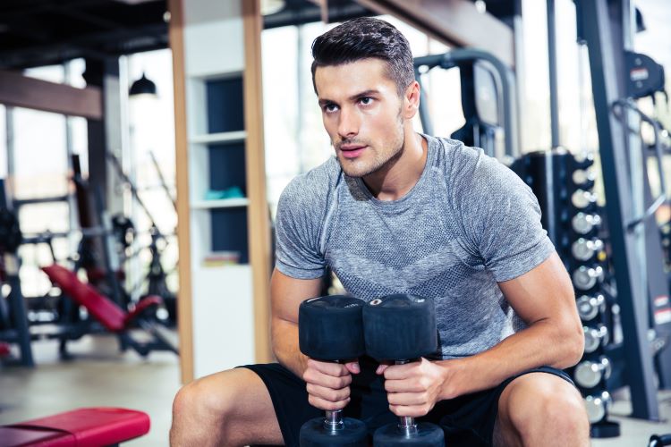 Man sitting in a gym holding dumbbells