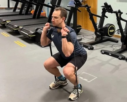 Man in a gym performing a resistance band squat
