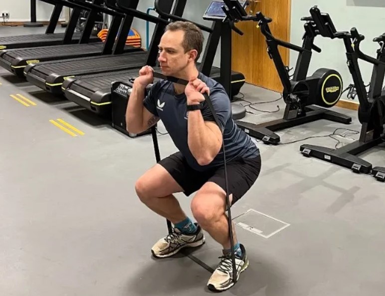 Man in a gym performing a resistance band squat