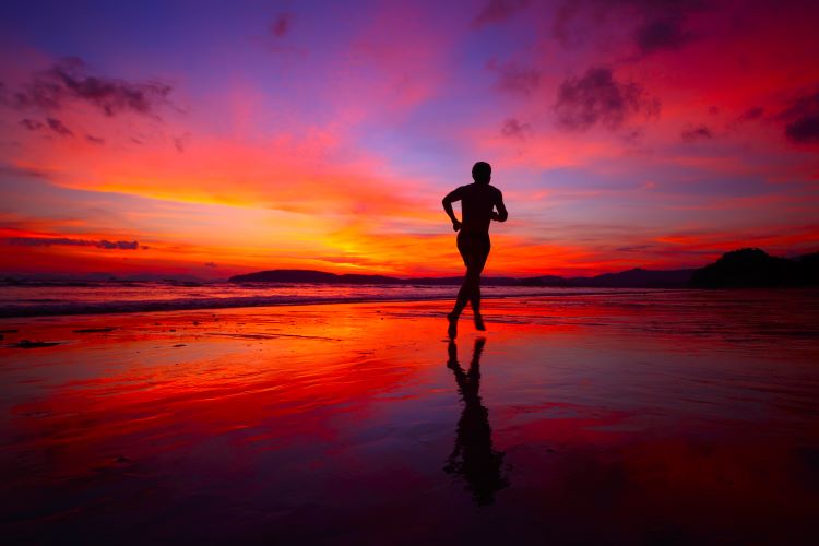 Silhouette of a man running along a beach at sunset