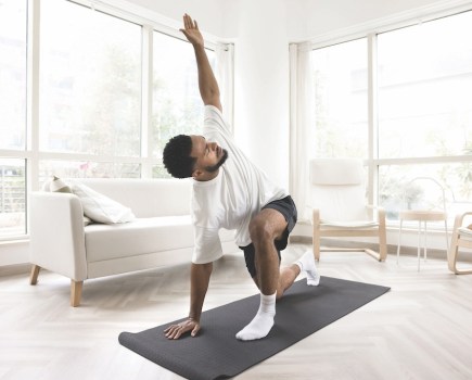 Serious young Black man doing morning exercises at home, keeping twisting yoga asana on mat, caring for wellness, fit, wellbeing, healthy active lifestyle, training body in apartment