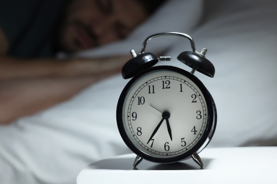 Man sleeping in bed, focus on alarm clock