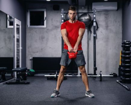 Man in a red t-shirt swinging a kettlebell in a gym