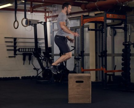 Man performing a box jump in a gym