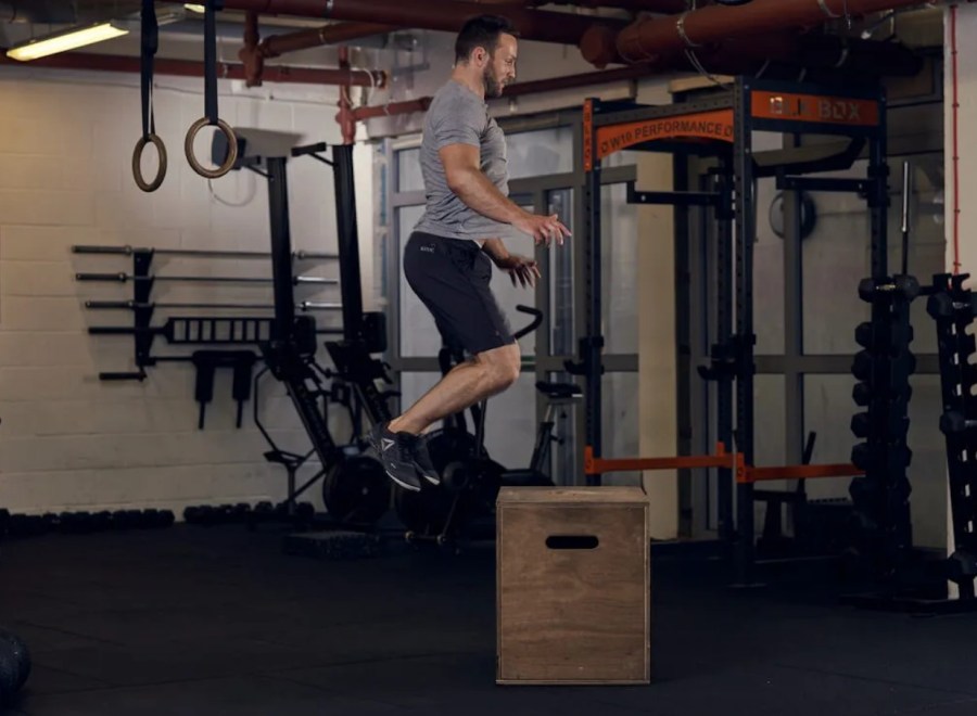Man performing a box jump in a gym