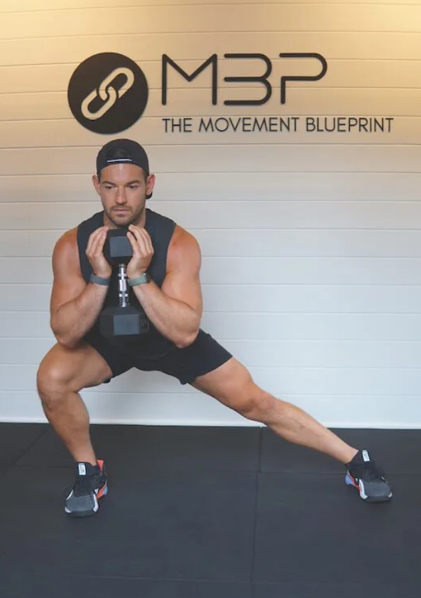 Man in a gym performing a frontal plane lunge with a dumbbell