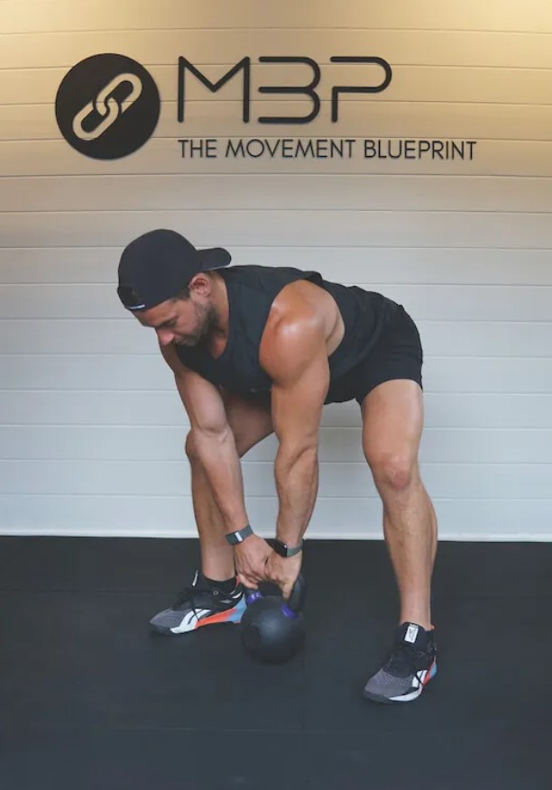 Man in a gym performing a kettlebell sumo deadlift