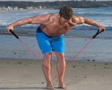 Man on a beach performing a banded bent-over row